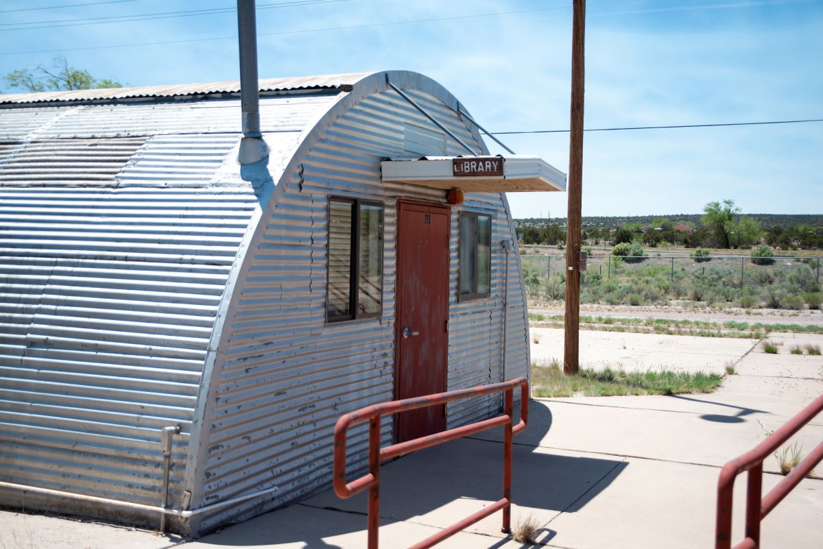 A small, old modular building with a door, once used as a library, stands quietly in a peaceful setting.