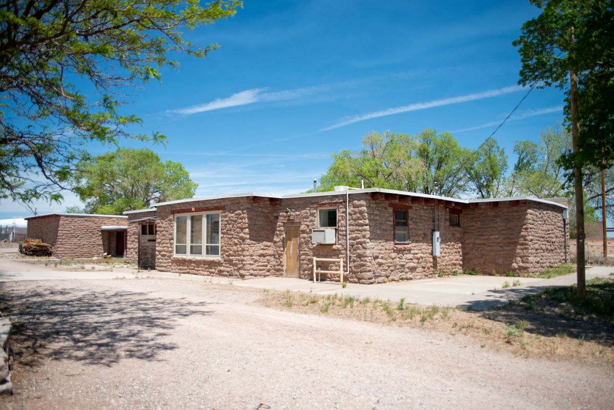 A small brick building stands on a dirt road, once part of the school that held classrooms, a dining room, kitchen, library, and counseling room.