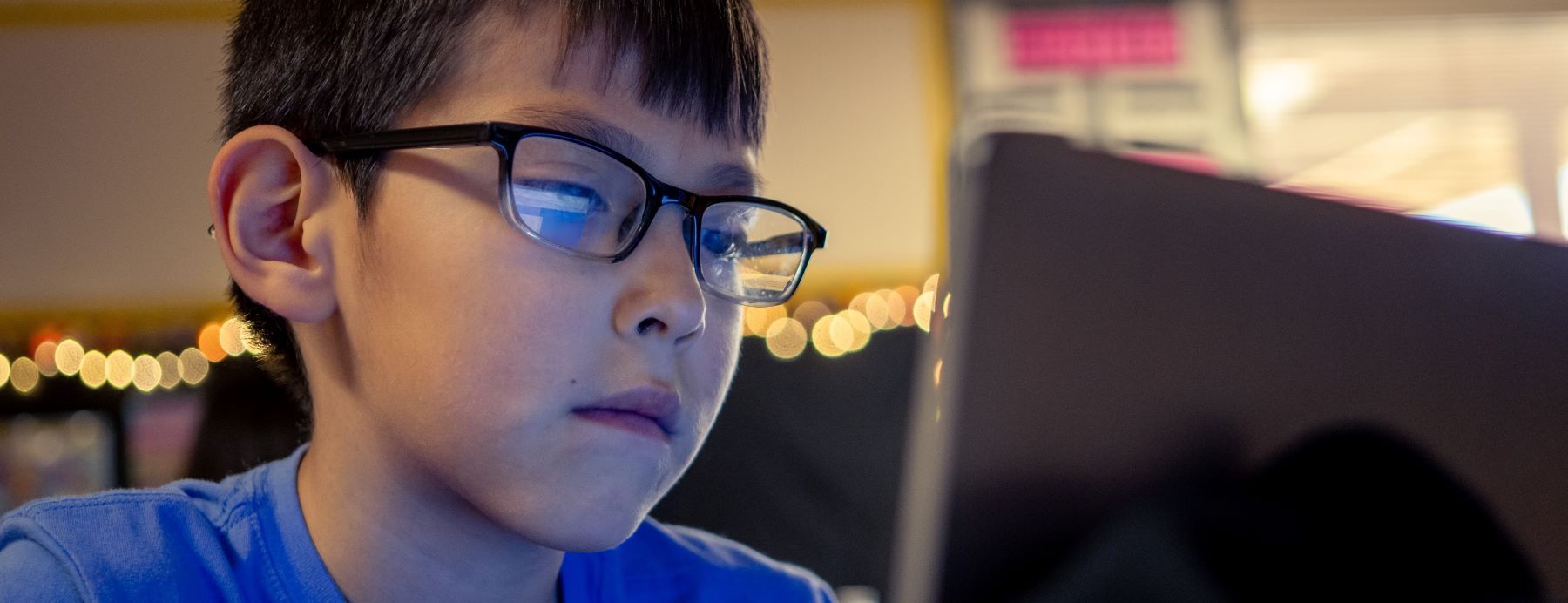 A student with glasses is focused on a laptop screen.